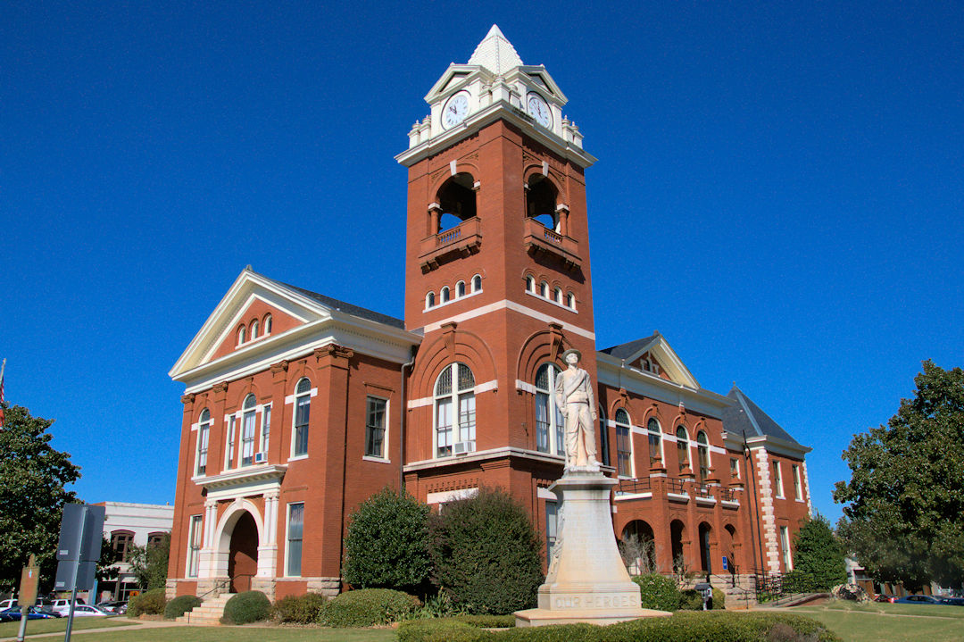 The historic red-brick Butts County Courthouse with its clock tower on the square in Jackson, Georgia, under a clear blue sky